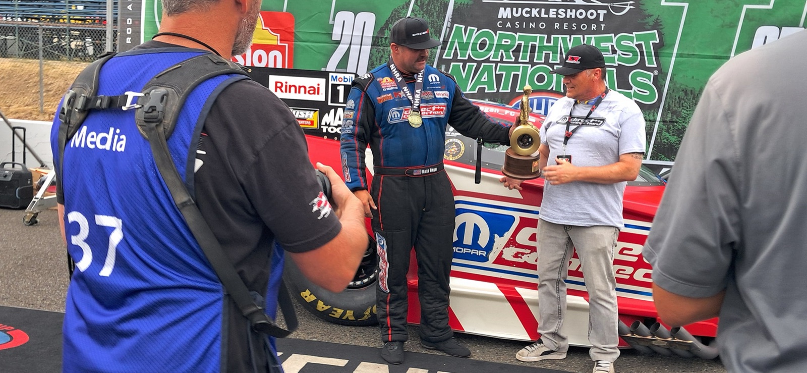 Matt Hagan handing off the Northwest Nationals trophy to JOEY on the track at Pacific Raceways, Muckleshoot Casino Resort signage in the background.